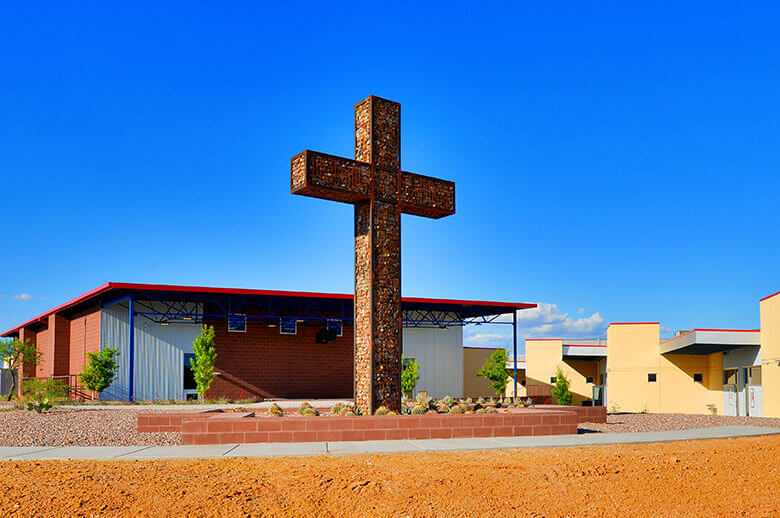A single story modern church build in the desert with a large metal cross in the front created by the architectural design team at Swaim Associates