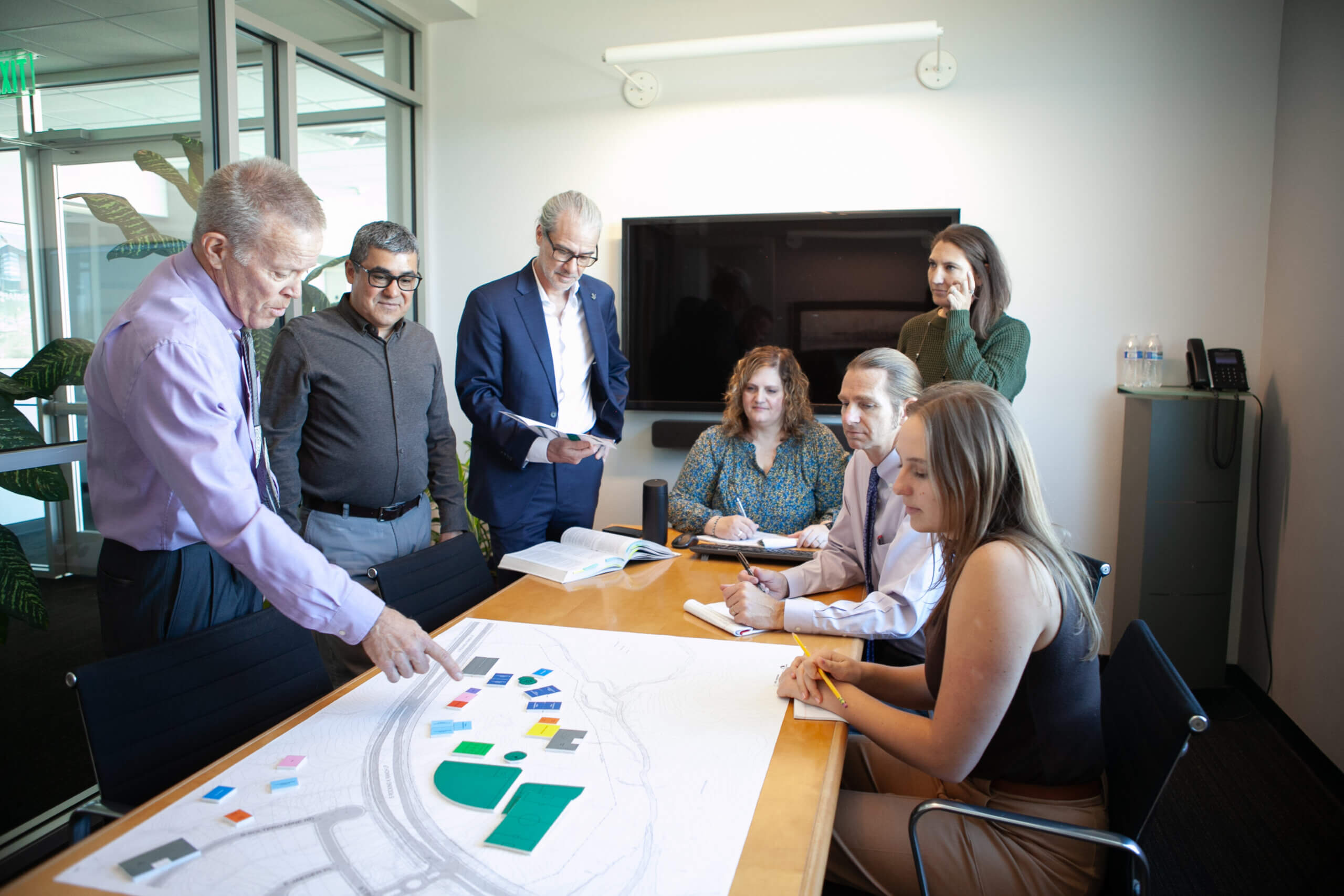 A team of architects sitting and standing around a conference table discussing architectural design on a large diagram